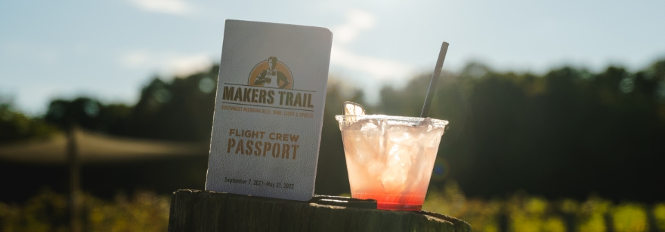 A mixed drink and a Makers Trail passport sitting on a wooden post.